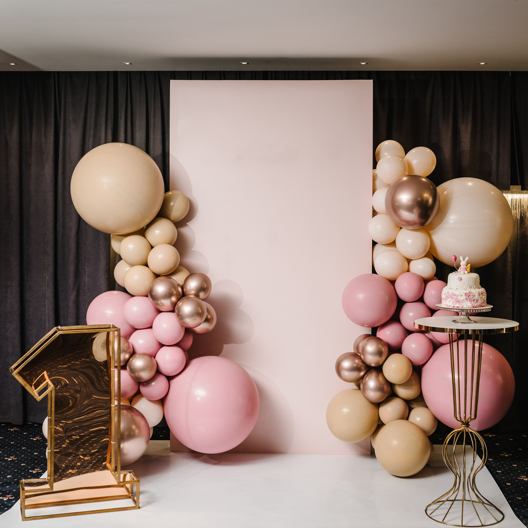 Arch decorated with pink, brown, and gold balloons. Trendy Cake for a girl. Copy space. Birthday Cake for 1 year on a background photo wall. Delicious reception at a birthday party.