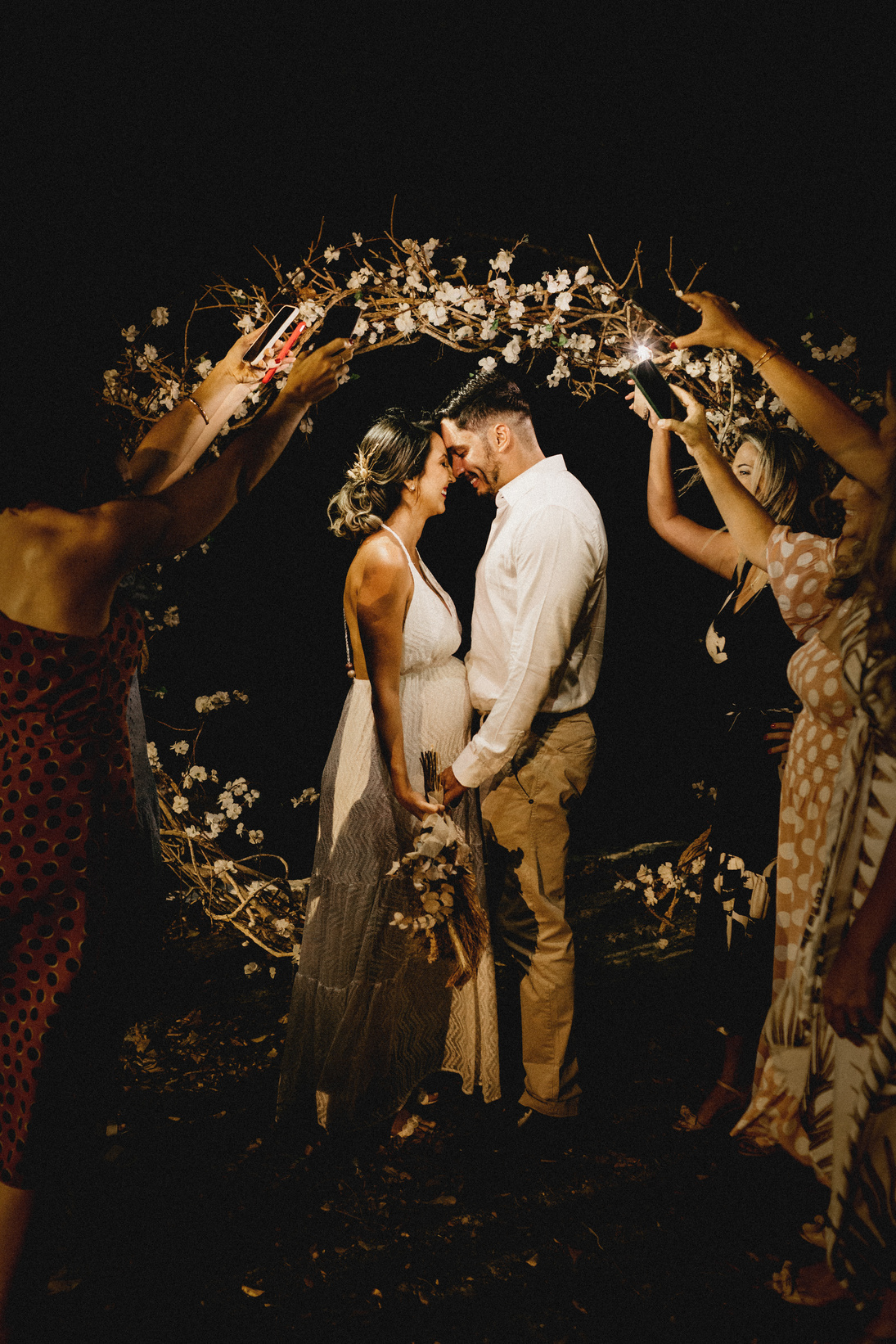 Cheerful couple kissing near guests holding decorative wreath at wedding